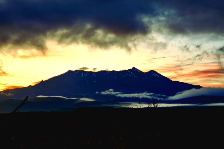 a sunset over a body of water with a mountain in the background