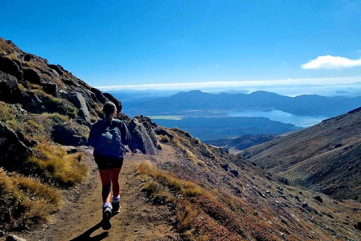 Person hiking on mountain trail with scenic lake view.